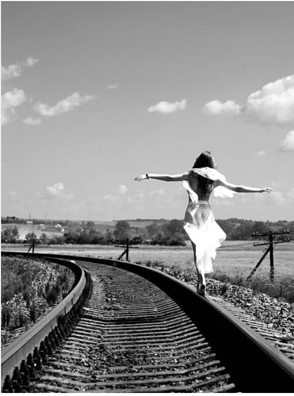 Woman walking on train tracks with arms outstretched